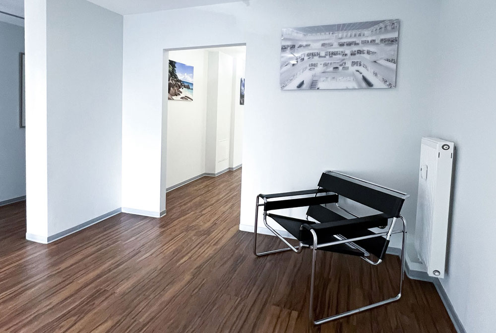 ehandlungszimmer der Zahnarztpraxis Dirk Alda in Niederkassel bei Bonn, mit Holzfussboden, hochwertiger technischer Einrichtung, warmen Farben und Flatscreen.
