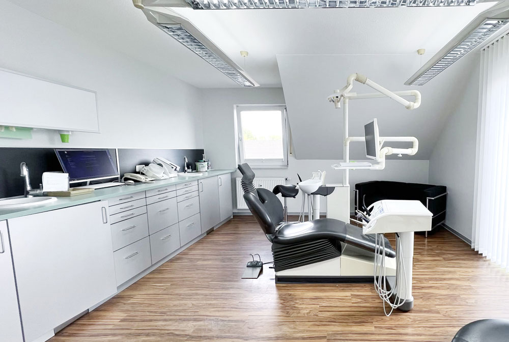 Behandlungszimmer 2 der Zahnarztpraxis Dirk Alda in Niederkassel bei Bonn, mit Holzfussboden, hochwertiger technischer Einrichtung, warmen Farben und Flatscreen.