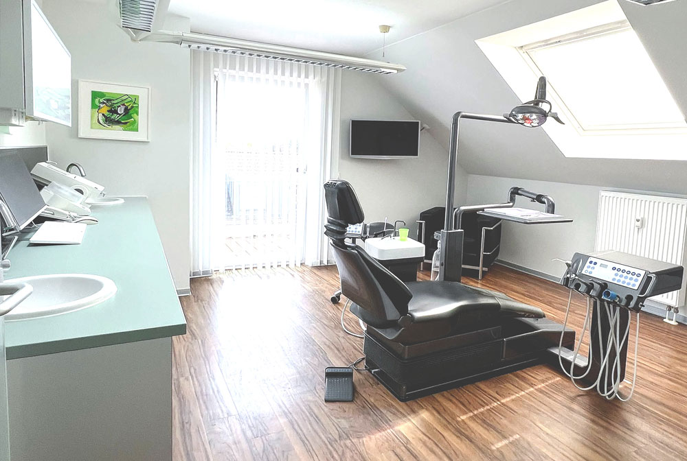 ehandlungszimmer der Zahnarztpraxis Dirk Alda in Niederkassel bei Bonn, mit Holzfussboden, hochwertiger technischer Einrichtung, warmen Farben und Flatscreen.